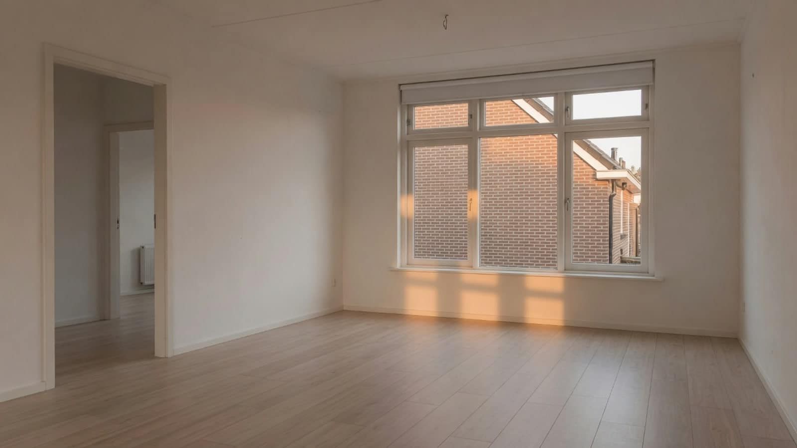Ruime lege woonkamer met groot raam, in warm laag licht
