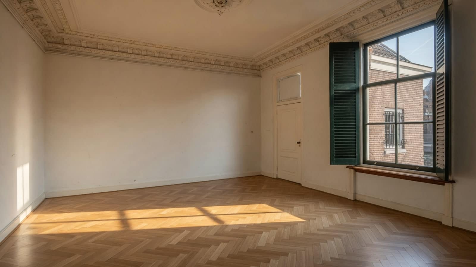 Lege kamer met kroonlijst en luiken, met de late zon over het visgraatparket