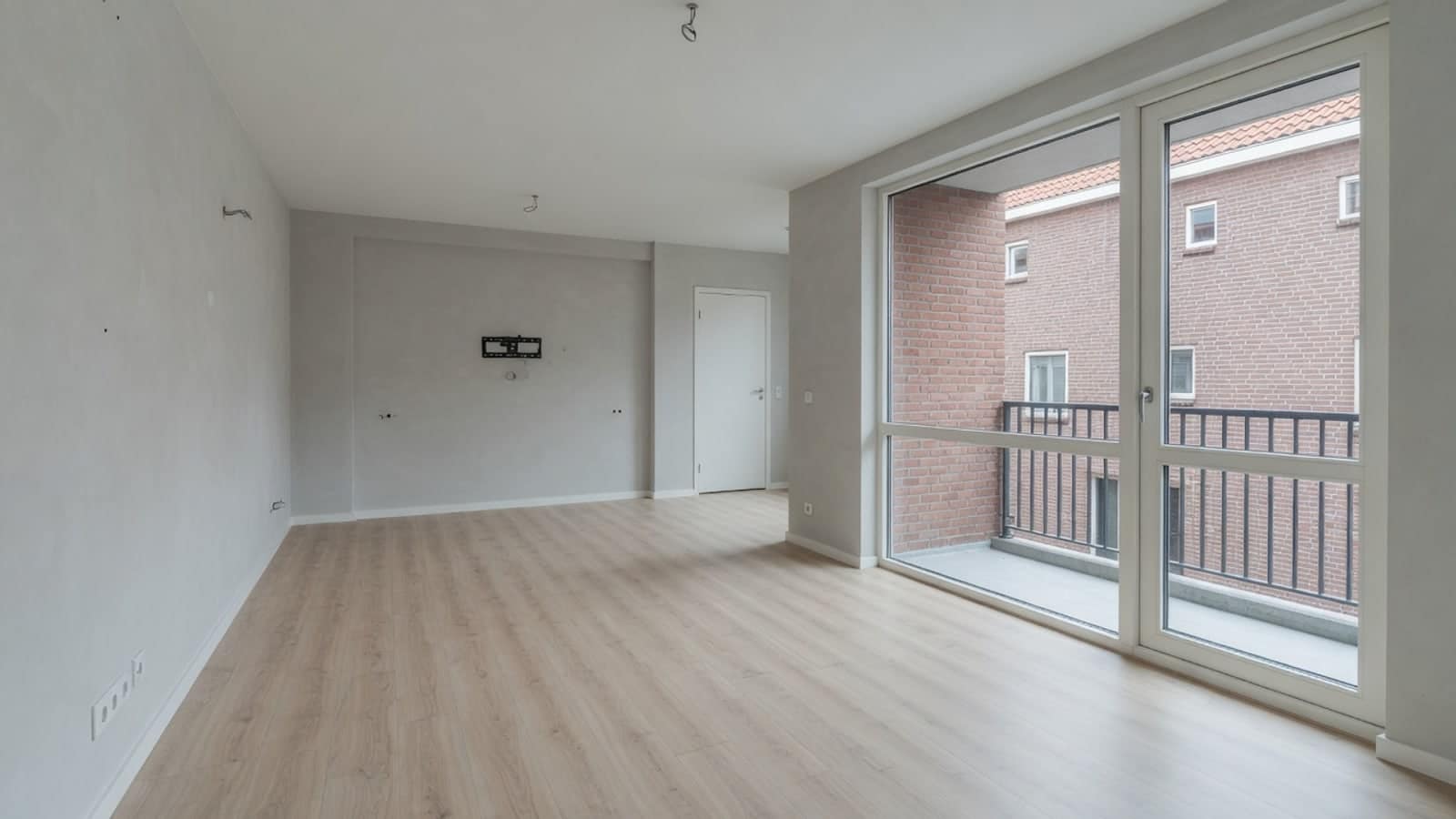 Leeg appartement met schuifpui naar het balkon en lichte laminaatvloer