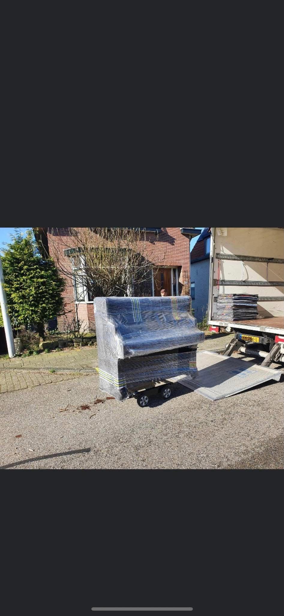 Ingepakte piano op de rijplaat naast de neergelaten laadklep van de wagen
