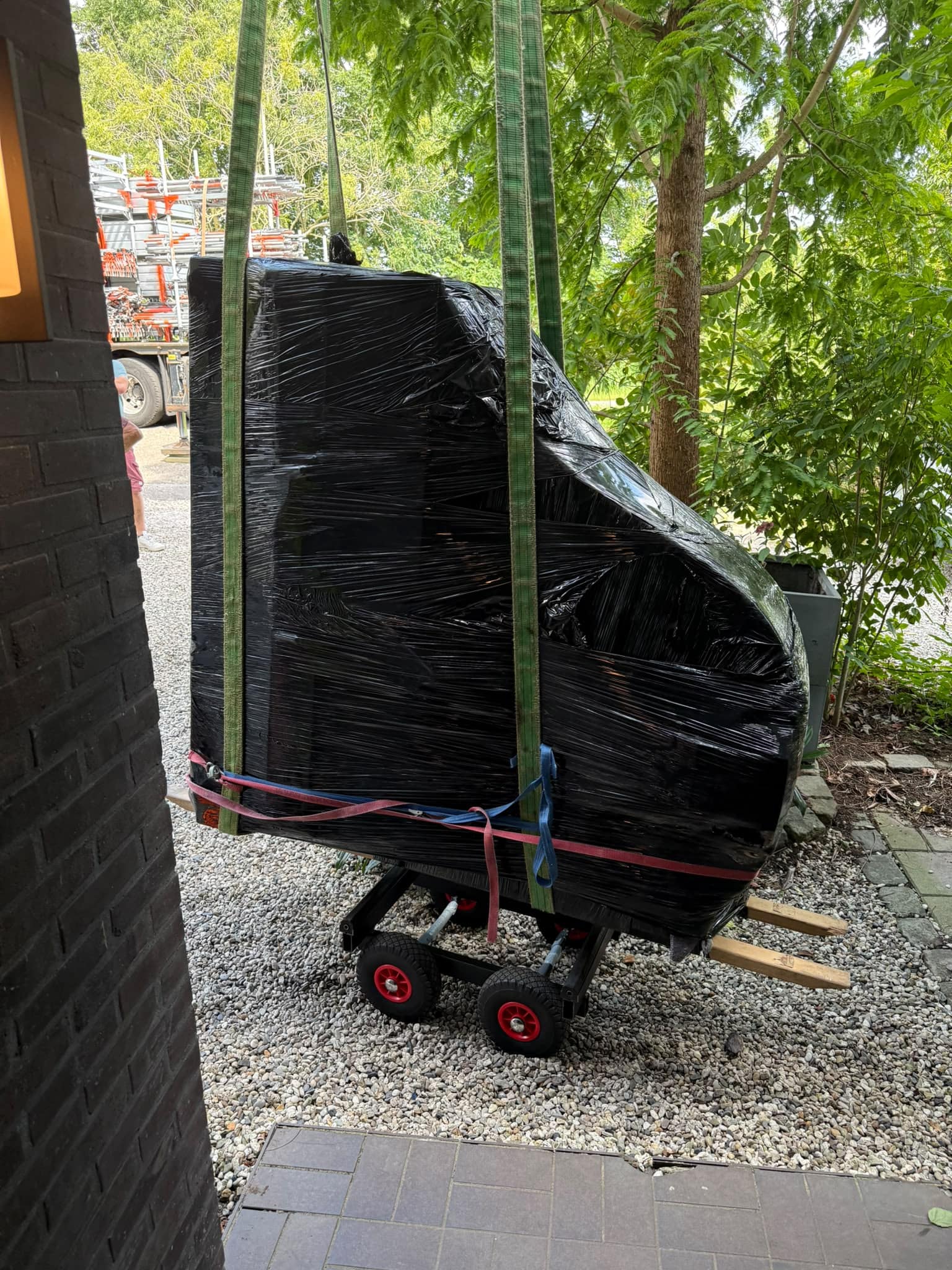 Vleugel in zwarte folie aan hijsbanden boven een pianowagen met luchtbanden