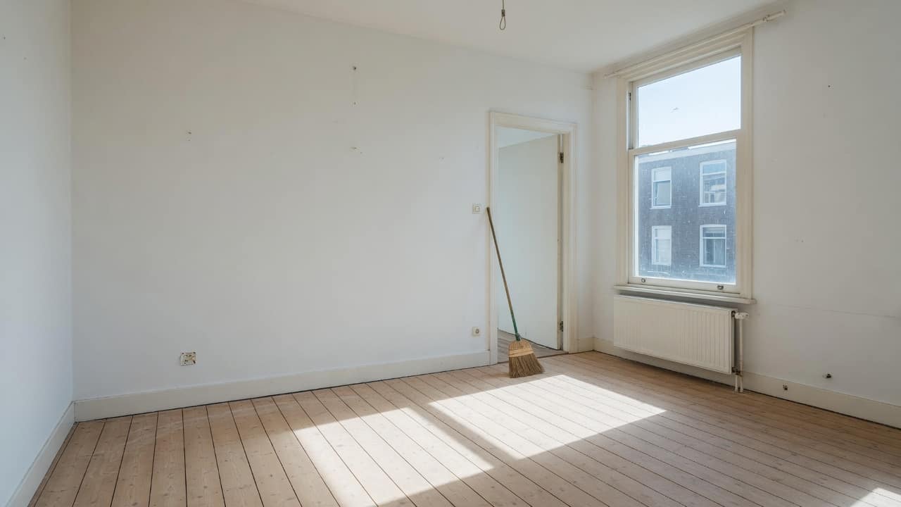 Leeggeruimde kamer met bezemschone vloerdelen en een bezem tegen de deurpost