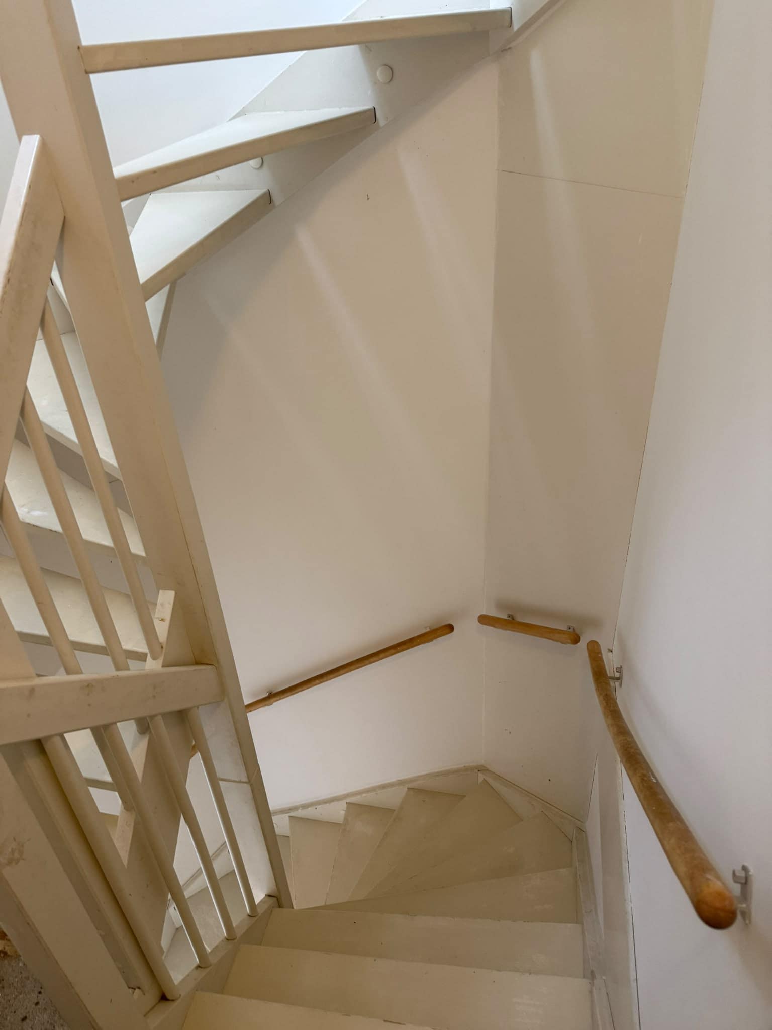 Wit geschilderd trappenhuis met houten leuningen langs de muur