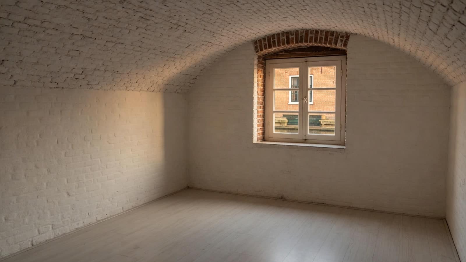 Leeg gewelfd kelderruim met warm licht door een klein diep raam