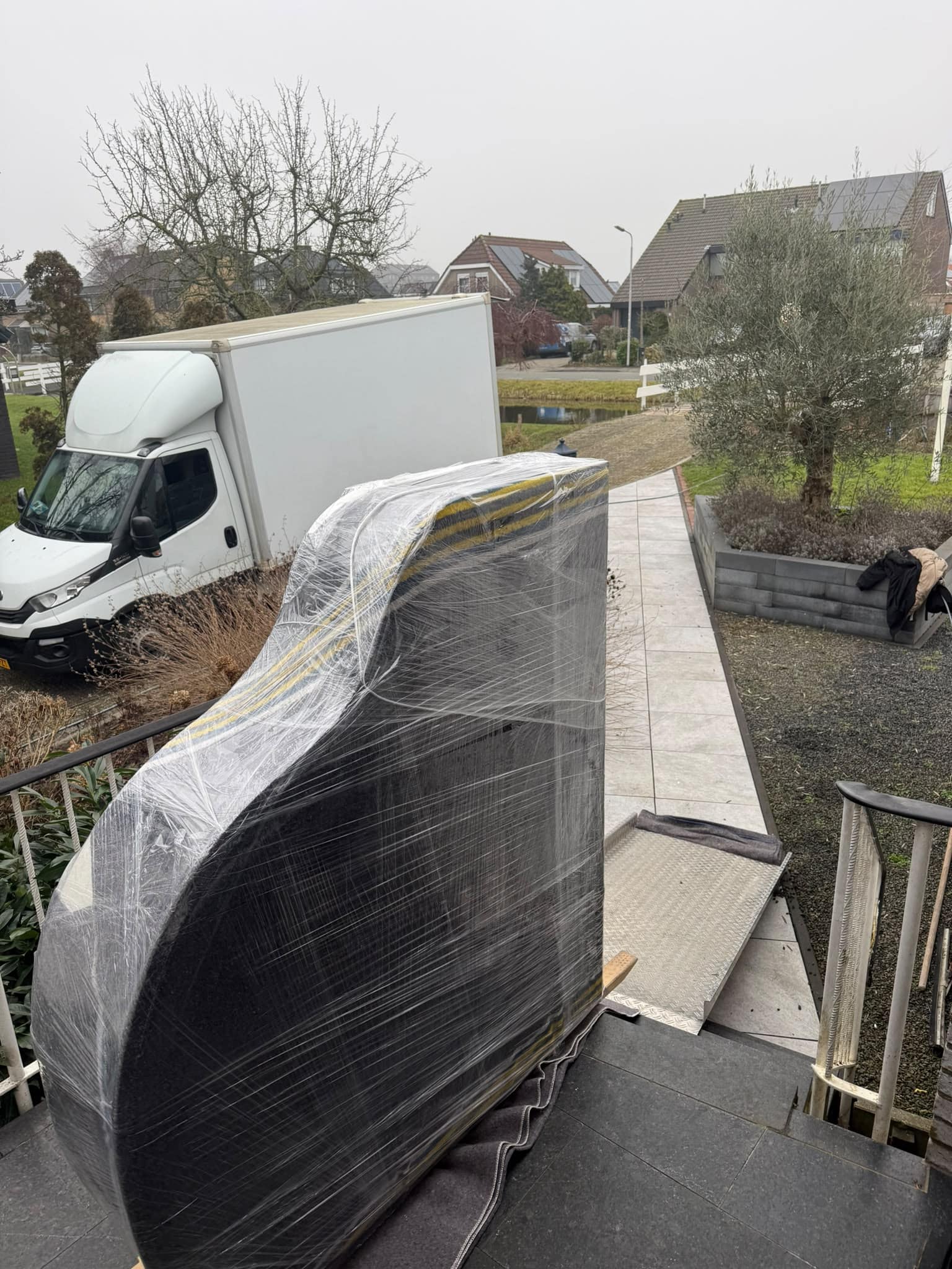 Vleugel in krimpfolie op een rijplaat, klaar om over het tuinpad naar de wagen te gaan